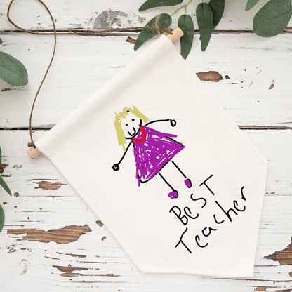 Canvas with a child's drawing of a girl in a purple dress and 'Best Teacher' text on a wooden surface with greenery. | Little Heirloom