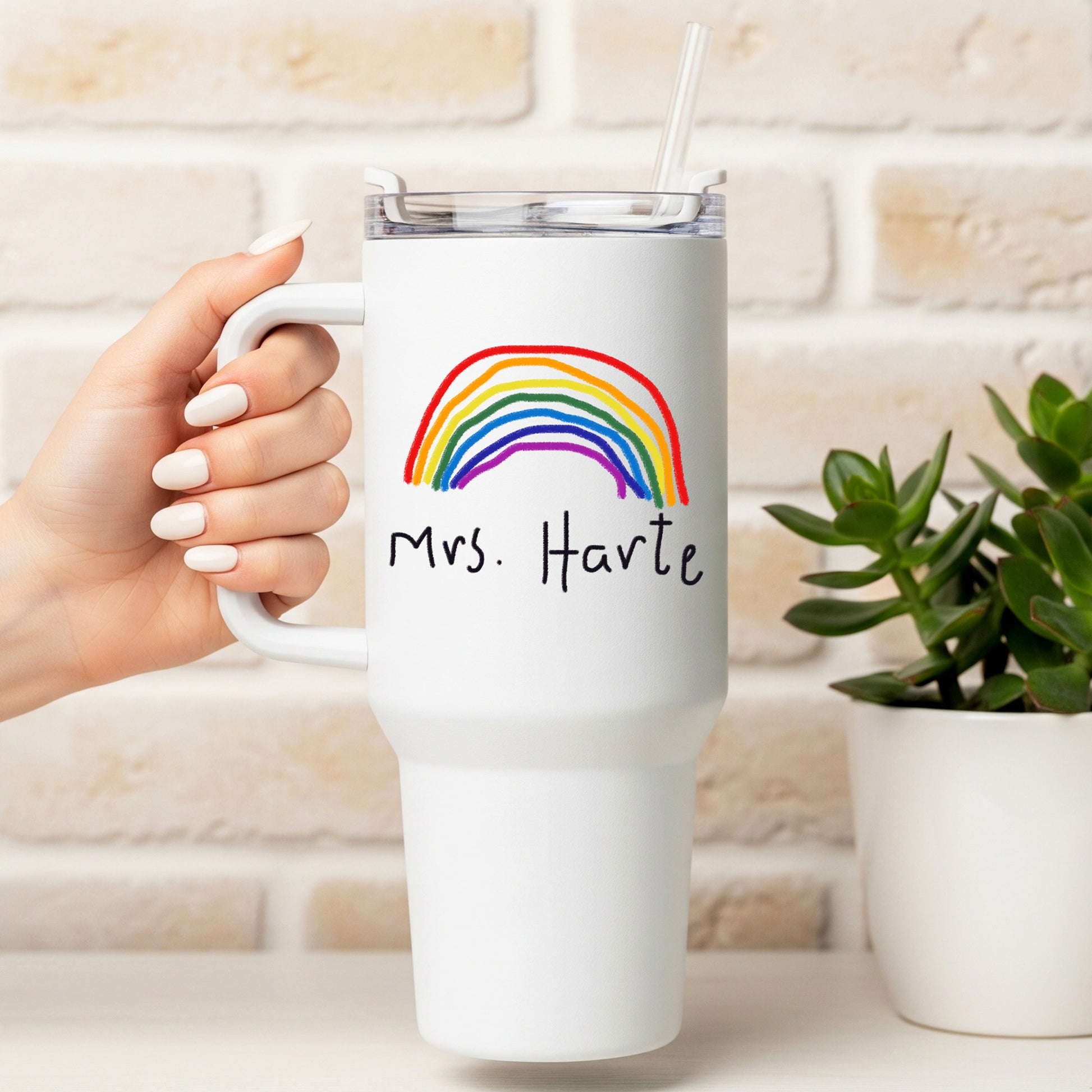 White mug with rainbow and 'Mrs. Harte' text held by a hand, against a light brick wall background. | Little Heirloom