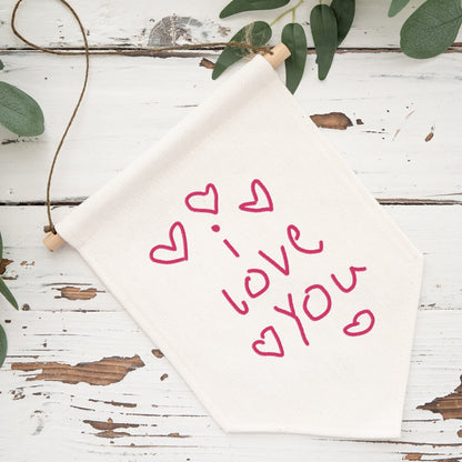 White fabric with 'I love you' text and hearts on a rustic wooden surface with greenery. | Little Heirloom
