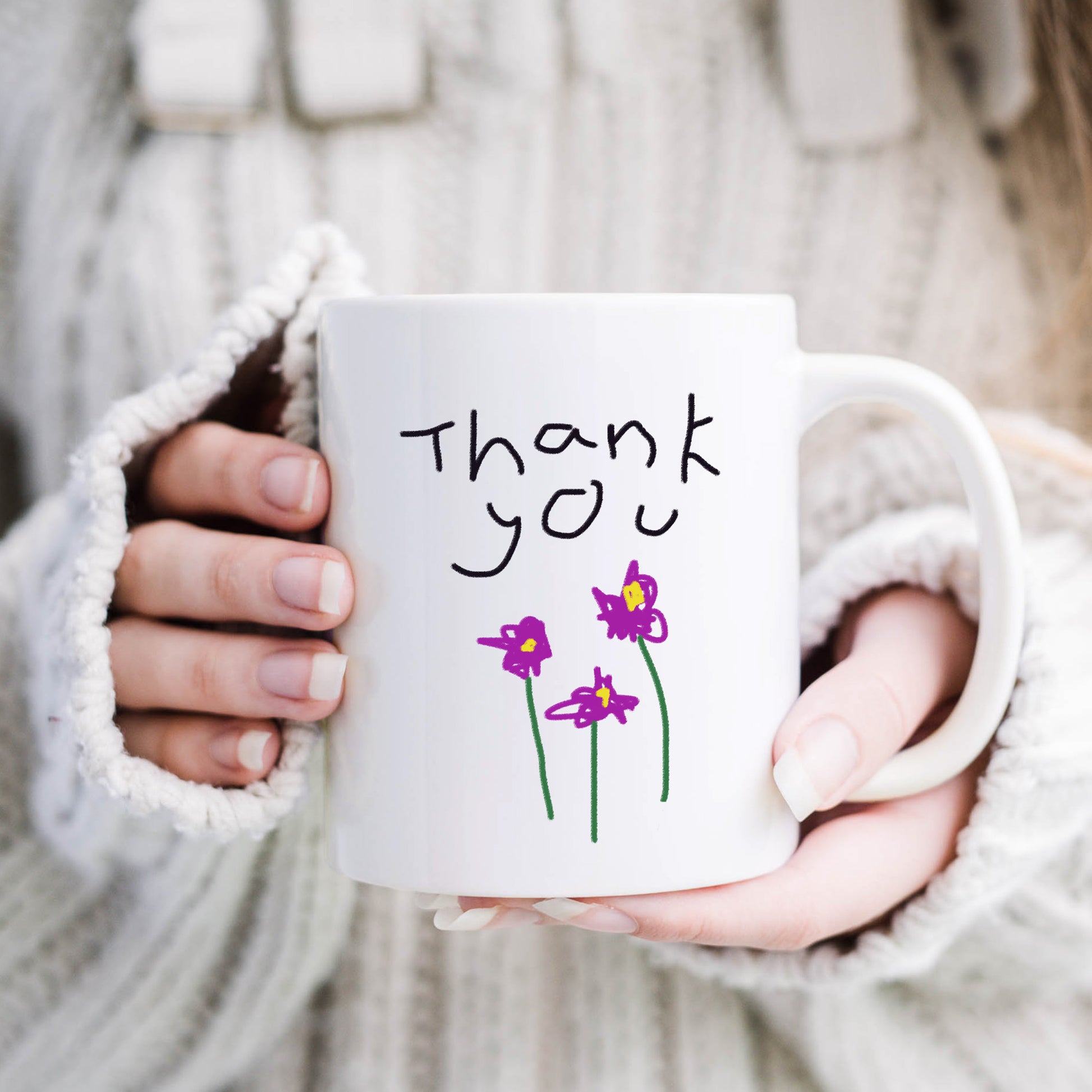 Person holding a white mug with 'Thank you' and flower drawings, wearing a white sweater. | Little Heirloom