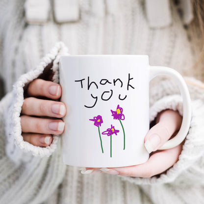 Person holding a white mug with 'Thank you' and flower drawings, wearing a white sweater. | Little Heirloom